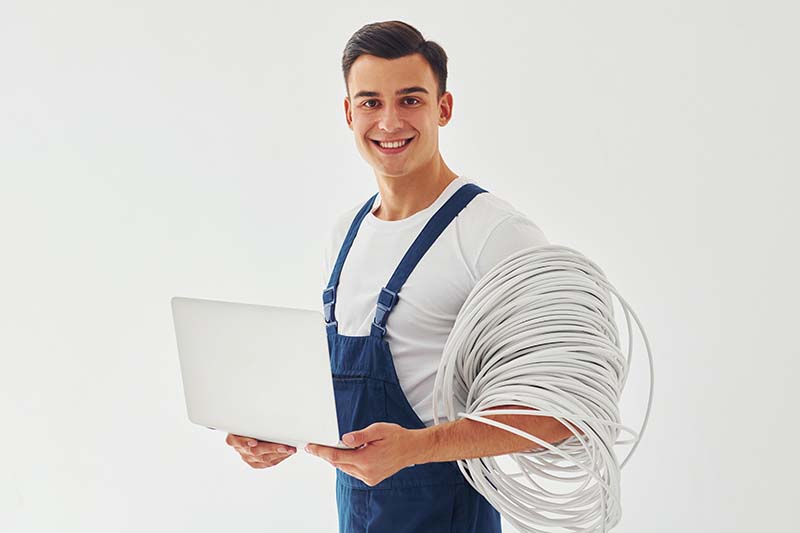 Uses laptop. Male worker in blue uniform standing inside of studio against white background